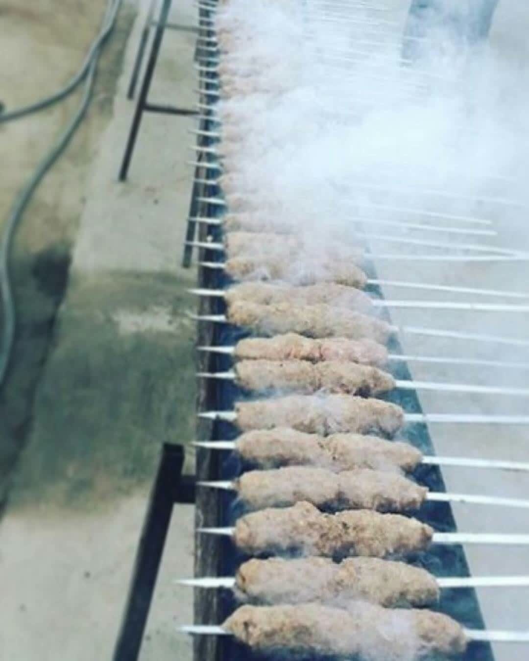 A rank of kebabs on long skewers above the grill